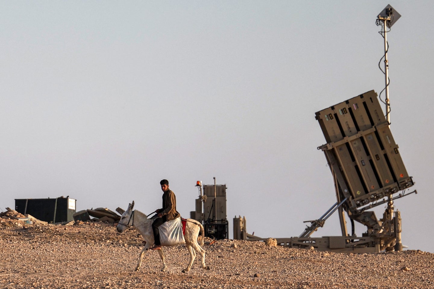 A boy rides a donkey near one of the batteries of Israels Iron Dome missile defence system at a village not recognised by Israeli authorities in the southern Negev desert on April 14, 2024. (Photo by AHMAD GHARABLI / AFP) (Photo by AHMAD GHARABLI/AFP via Getty Images)